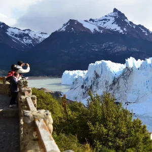 Familia fotografiando el glaciar Perito Moreno desde las pasarelas con montanas nevadas y bosque en El Calafate